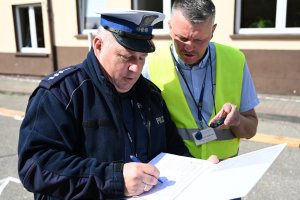 Na zdjęciu widać policjanta, który ocenia uczestników Turnieju. Młodzież zmaga się z kolejnym etapem konkursu, jakim jest jazda motorowerem.