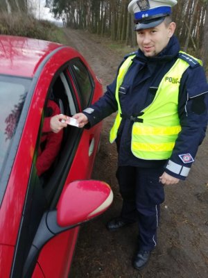 Na zdjęciu widać policjanta, prowadzącego kontrolę drogową. Na zdjęciu widać też fragment czerwonego pojazdu.