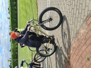 Na obrazie widać chłopca, jadącego na rowerze. rower koloru jasnego, chłopiec ubrany w czapkę i kurtkę. Zdjęcie wykonane podczas zdawania egzaminu na kartę rowerową