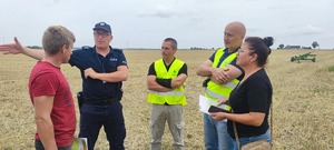 Na obrazie widać policjanta, przedstawiciela KRUS-u i PIP podczas wspólnych działań. Zdjęcie zostało wykonane na polu. Obok stoi pani.