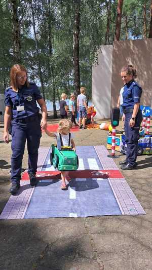 Na zdjęciu widać dwie policjantki, które pozują do zdjęcia wspólnie z dzieckiem, które jest w autochodziku.