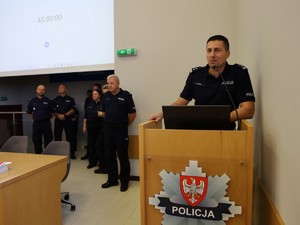 Przy mównicy stoi policjant w mundurze. Sytuacja ma miejsce na konkursie Policjant Wydziału Kryminalnego 2024