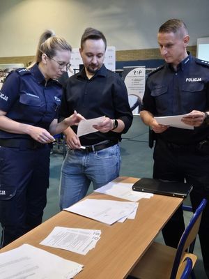 Na zdjęciu widać policjantkę i policjanta, którzy rozmawiają z mężczyzną. W ręku trzymają ulotki, dotyczące pracy w policji.