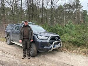 Na zdjęciu jest widoczny samochód straży leśnej i strażnik, który pozuje do zdjęcia