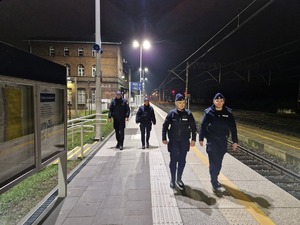 Na obrazie widać policjantki i funkcjonariuszy SOK na dworcu kolejowym w Pleszewie. Idą wzdłuż torów i patrolują teren.. Funkcjonariuszki są skierowane tyłem do zdjęcia