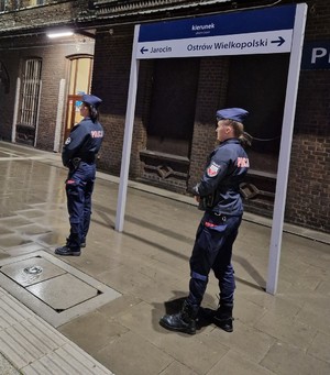 Na obrazie widać policjantki na dworcu kolejowym w Pleszewie. Stoją bokiem do zdjęcia..