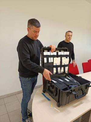 Na obrazie widać techników kryminalistyki, którzy prezentują walizkę kryminalistyczną. Spotkanie odbywa się w KPP w Pleszewie.