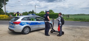 Policjanci rozmawiają z chłopakiem, który porusza się na hulajnodze. Obok stoi policjant i radiowóz.