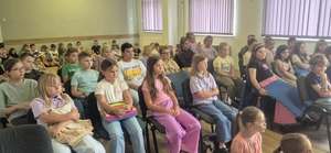 Na obrazie widać dzieci siedzące na krzesłach, które słuchają prelekcji policjantki