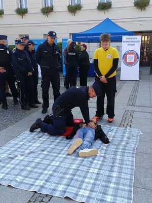 Na obrazie widać policjanta, który prowadzi resuscytację na fantomie. W tle widać innych uczestników akcji.