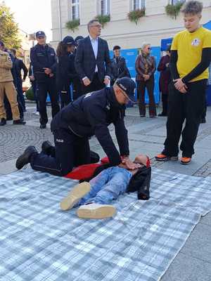 Na obrazie widać policjanta, który prowadzi resuscytację na fantomie. W tle widać innych uczestników akcji.