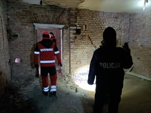 Zdjęcie wykonane w pustostanie, na zdjęciu widać policjantkę, która świeci latarką, na drugim planie widać ratownika.