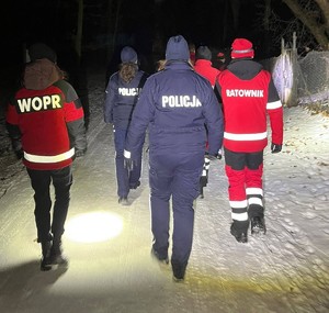 Na obrazie widać dwóch policjantów, zdjęcie jest zrobione od tyłu. Na zdjęciu są również ratownicy WOPE. Zdjęcie wykonano podczas akcji skierowanej na pomoc bezdomnym.
