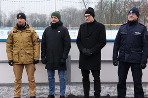 Na obrazie widać przedstawicieli służb, którzy są na pleszewskim lodowisku. Stoją obok siebie. Wśród nich policjanci, strażacy, urzędnicy.