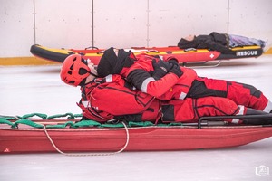 Na obrazie widać ratowników, którzy na sztucznym lodowisku robią pokaz wyciągania kogoś z wody