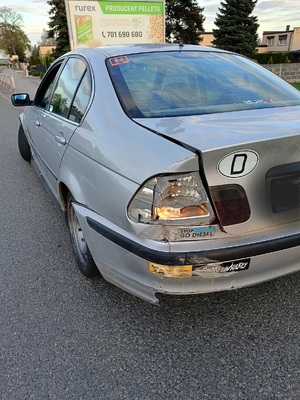 Na obrazie widać samochód marki BMW koloru jasnego, który ma łyse opony i uszkodzone reflektory