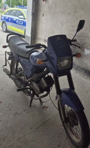 Motorower w garażu koloru niebieskiego a w tle radiowóz koloru niebiesko-żółtego